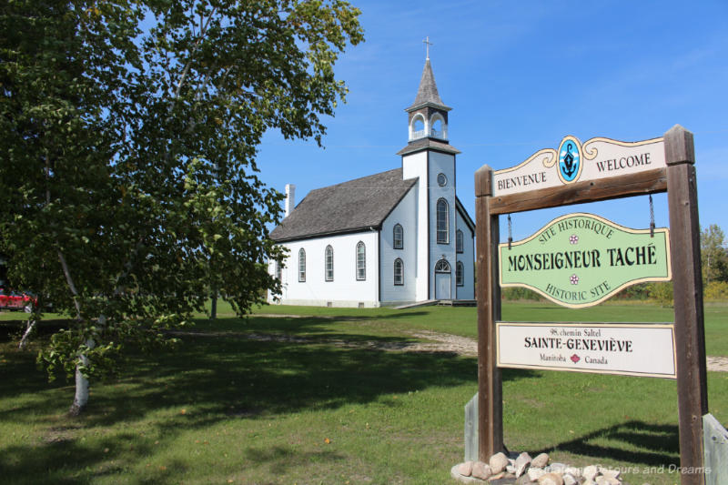 White wooden church with front steeple and sign indicating it is the Monseigneur Tache Historic Site