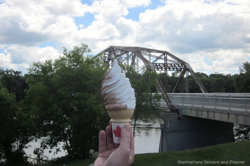 Ice cream cone with a view of a river bordered by trees and a steel-truss bridge in the background