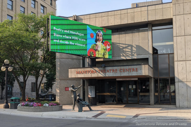 Front of brutalist style Manitoba Theatre Centre with a sculpture of two men in front of it