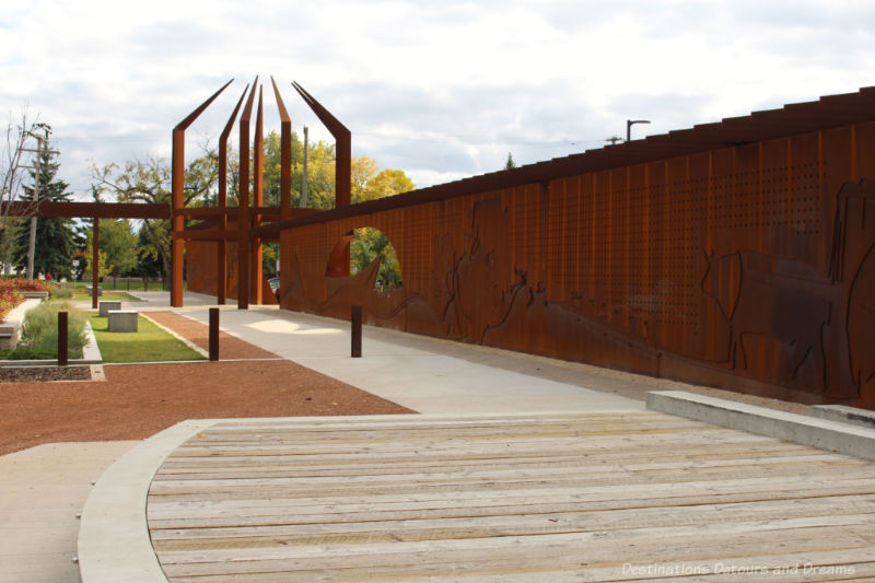 Walkway in a park with raised beds bordered by an metal interpretative wall at Upper Fort Garry