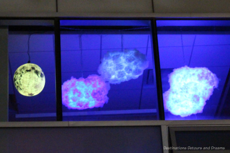Art display of a lit-up moon and three clouds changing colours