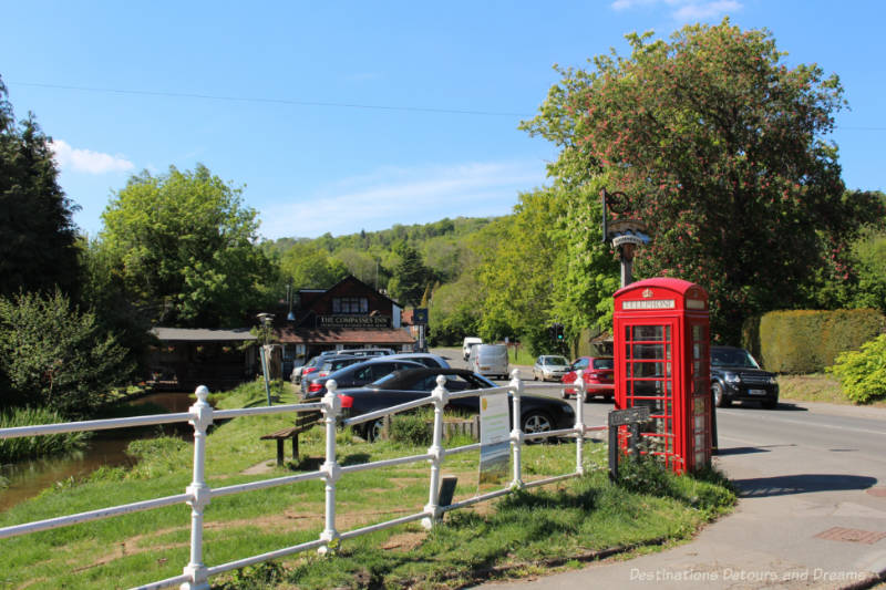 The Compasses Inn English country pub alongside a small river in Gomshall near an intersection with a red telephone box in the foreground