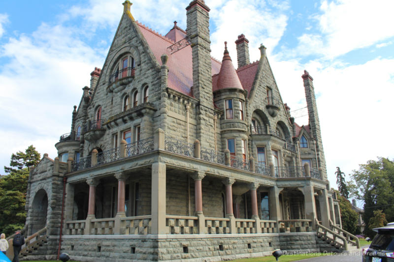 Stone castle-like mansion with threee stories, red tiled roof, stained glass windows and wraparound veranda with red stone columns