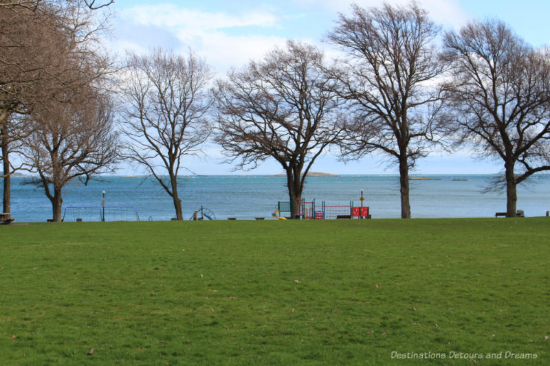 Grassy area with playground in front of the water at Willows Beach in Victoria, BC