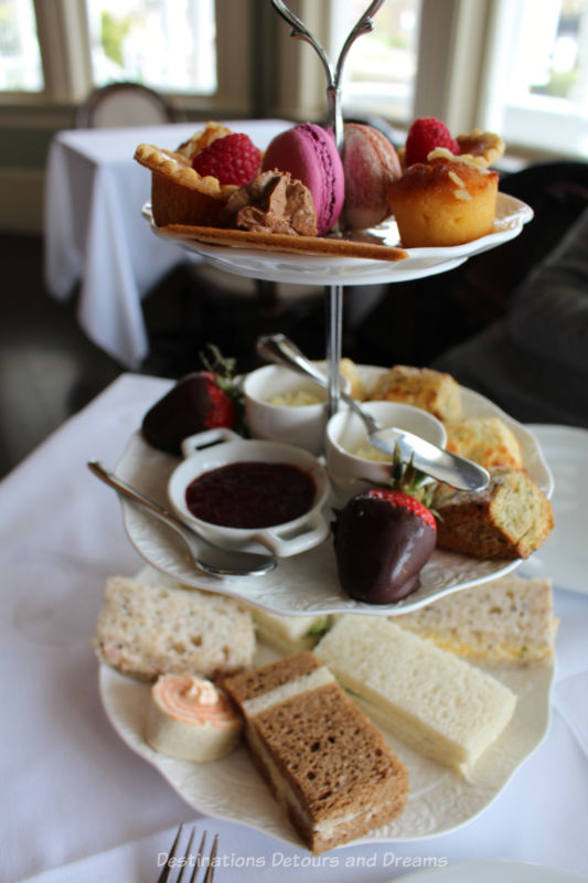 Three tiered plate with afternoon tea treats: fancy sandwiches, scones, and sweets