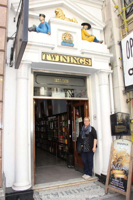 Standing in front of the entrance to London's Twining tea shop. White frame around the door with figures of two Oriental men and a lion resting on ledge above the door