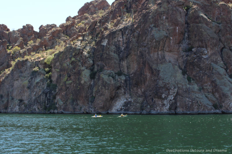 Two kayakers in the lake in front of a steep rock face