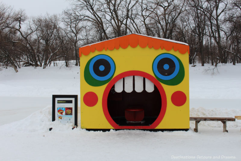 A bright yellow warming hut when a large red-rimmed mouth under two circular blue and green eyes form the entrance