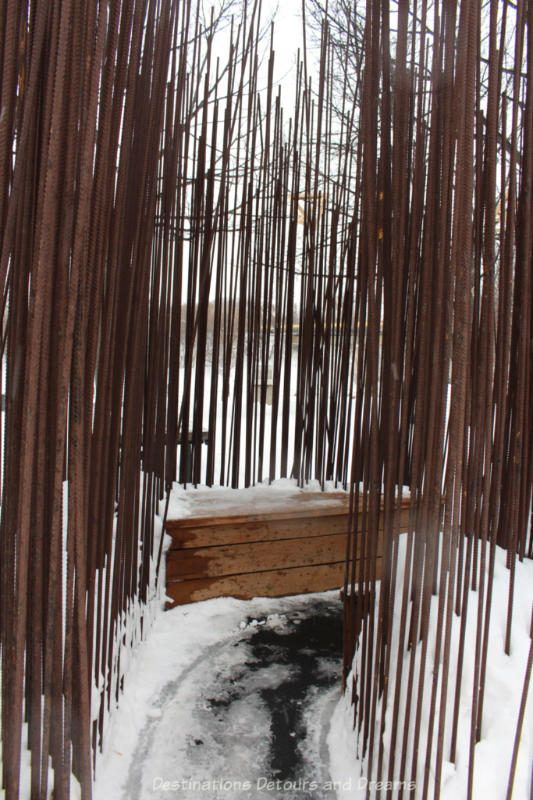Spikes of rebar provide a shelter leading into bench seating in a warming hut