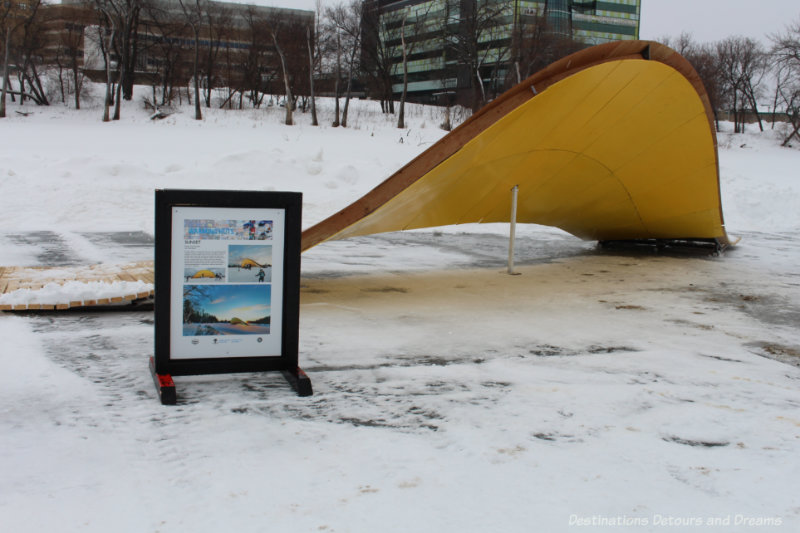 A yellow wedge-shaped warming hut on river in Winnipeg