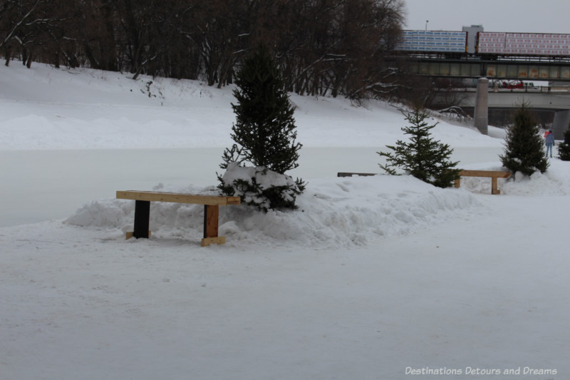 Wood benches spaced out alongside a frozen river skating trail