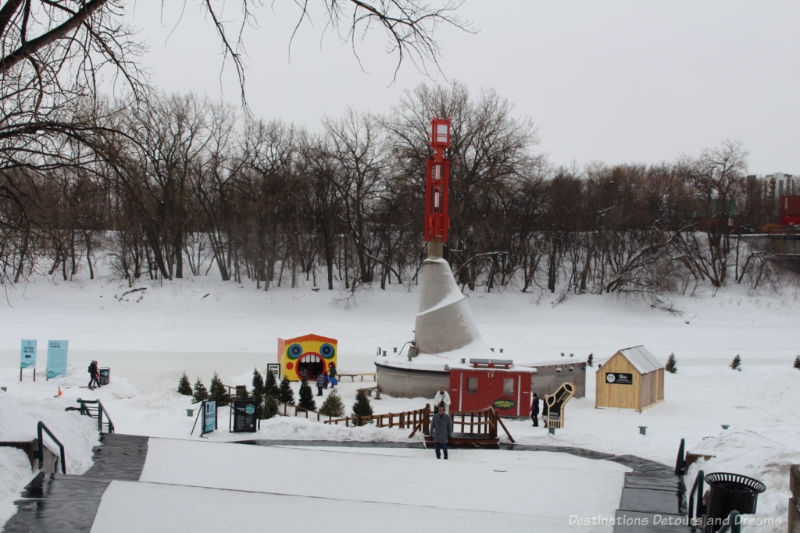 Steps down a snow slope to the frozen river where a couple of warming huts mark entrance to a skating trail in Winnipeg, Manitoba