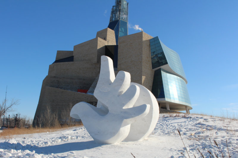 Snow sculpture of a hand with the towering stone and glass Canadian Museum for Human Rights behind it in Winnipeg, Manitoba, Canada: things to do in winter in Winnipeg