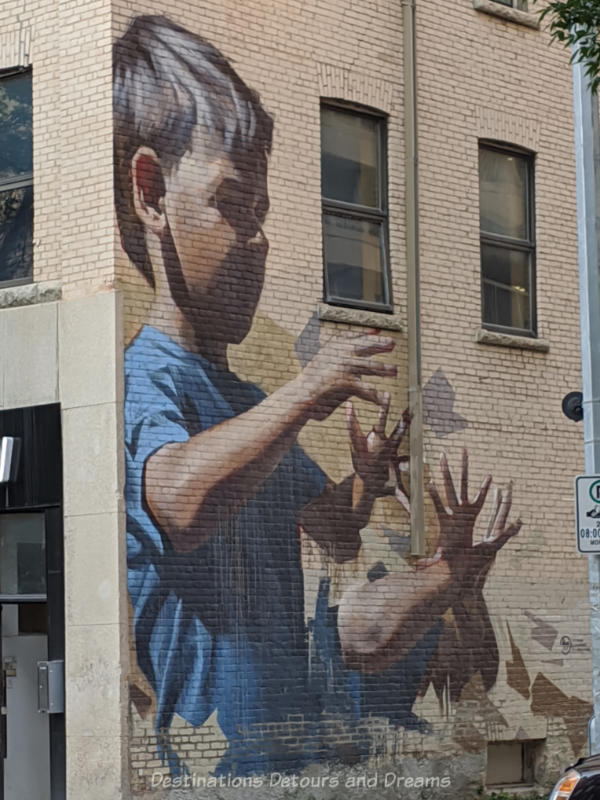 Mural on the side of a brick build showing a boy in a blue t-shirt with hands up and out