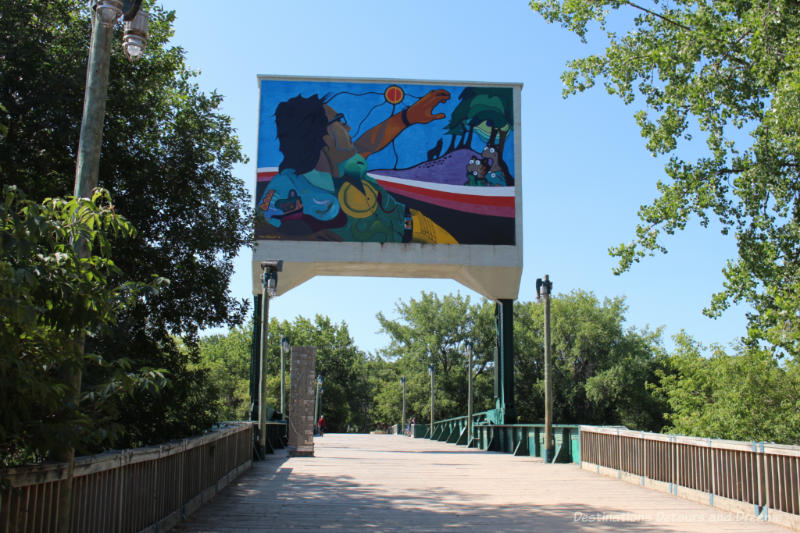 Vibrant coloured mural showing island with animals and man in canoe placed a bridge posts over pedestrian bridge at The Forks, Winnipeg