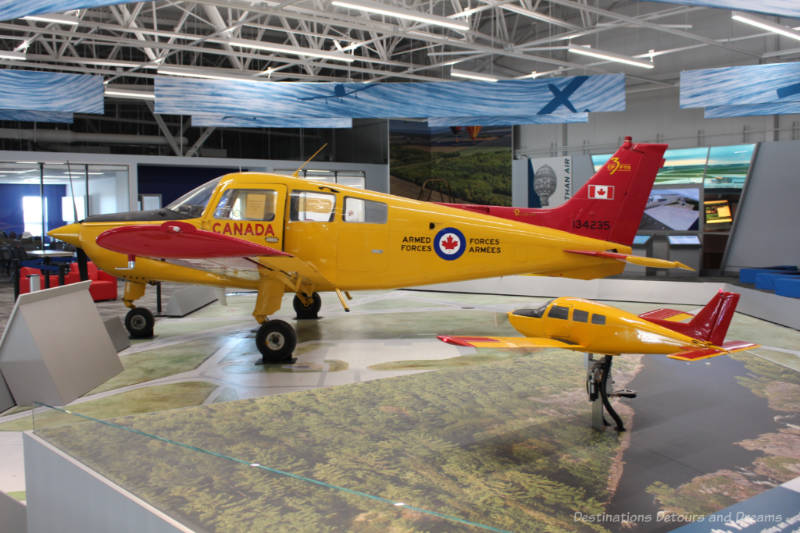 Yellow Armed Forces plane and smaller model of it on display at the Royal Aviation Museum of Western Canada
