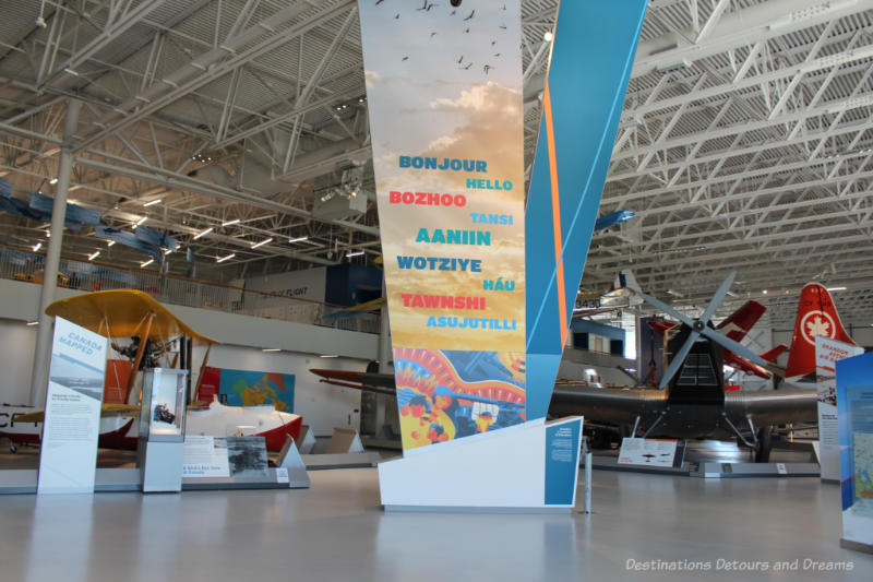 Sign saying welcome in several languages in front of various aircraft on display at the Royal Aviation Museum of Western Canada