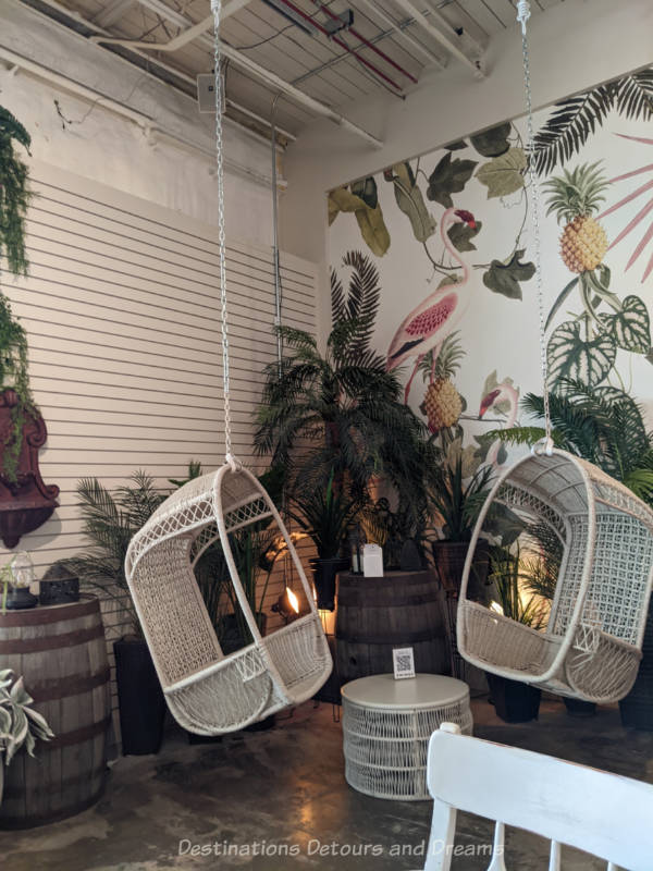 White wicker hanging chairs amid greenery and wooden kegs used as tables at Kilter Brewing