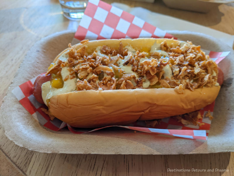 Hot dog topped with mango salsa, poblano mayo, and crispy onions