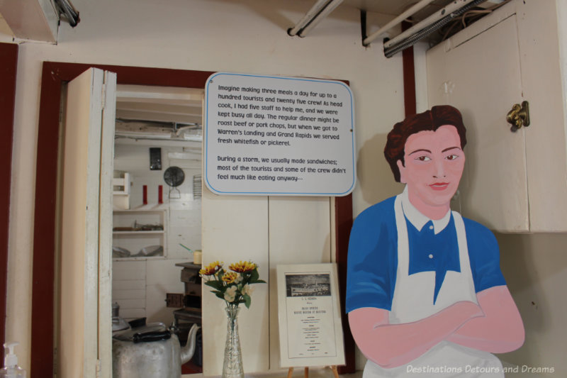 Cardboard figure of a cook in a museum old steamship galley in front of a sign describing her experrience
