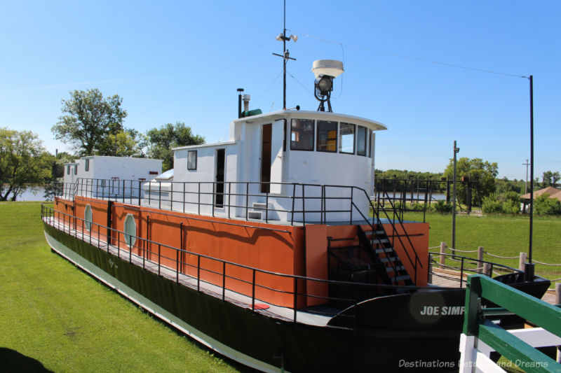 Flat-bottom 1960s freighter ship with orange bottom and white above water level cabin