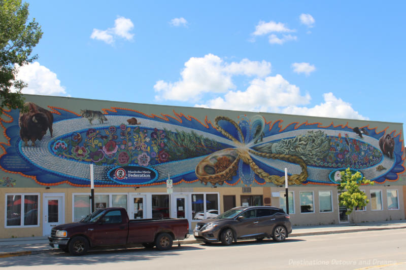 Intricate mural on the top half of building featuring the Métis symbol, beadwork motifs, the Four Medicines, and animal totems