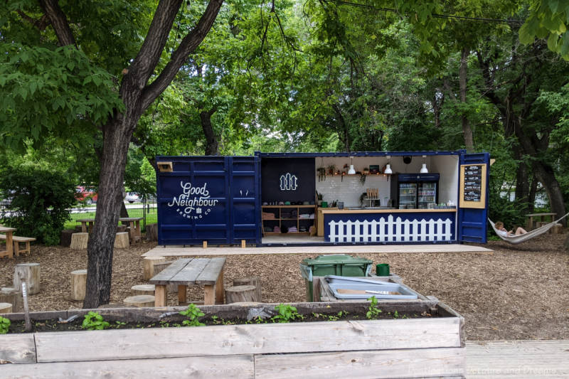Blue shipping container pop-up craft beer booth on patio area surrounded by mature trees.