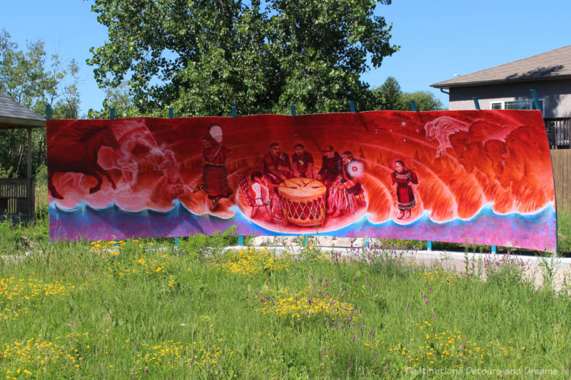 Mural in angry colours of red and purple depicts Indigenous people drumming with figures of animals (horses and bison) shaded into the red sky at the sides