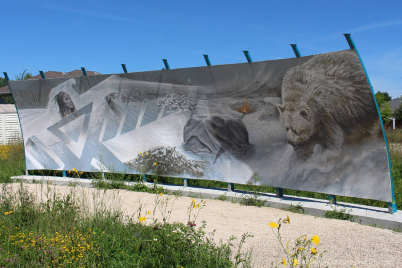 A mural in colours of mostly grey and white depicts a woman to one side trying to break through geometrical lines of white and several animals on ice and snow