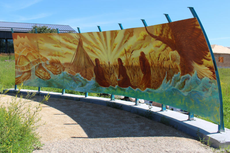 A autumn-coloured mural shows figure beside a tepee in a field of wheat with a waves of a sea below them and a large turtle to one side and an eagle to the other