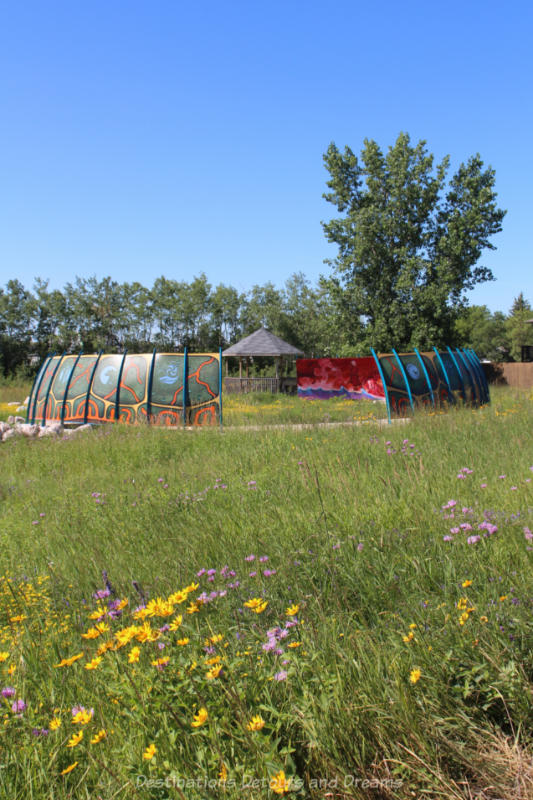 Curved panels painted with murals set in a circle in the midst of a tall grass prairie field