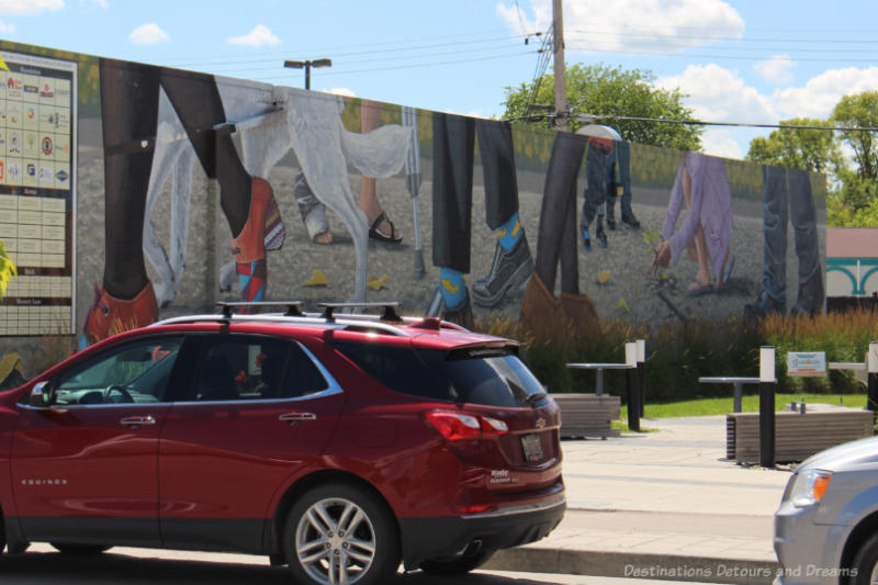 Mural on the side of a building showing the feet and lower legs of several people with the theme of don't judge me until you've walked a mile in my shoes.