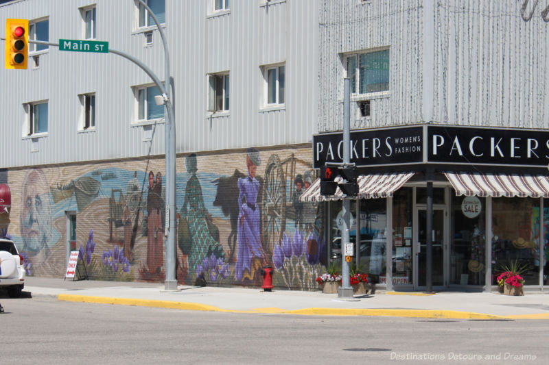 A murals on the side of a building featuring assorted women in dresses from days gone by amid purple crocuses blooming below