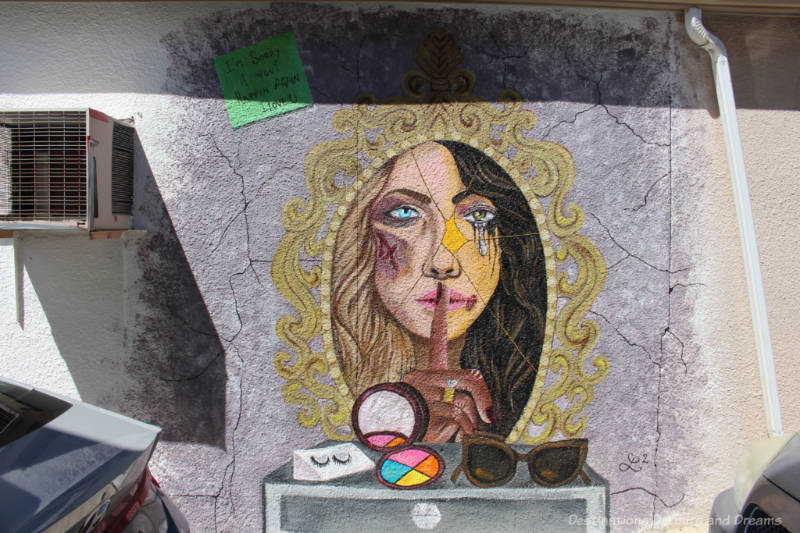 Mural showing a bruised woman's face inside a frame with a tear dripping and a finger indicating silence in front of her lips