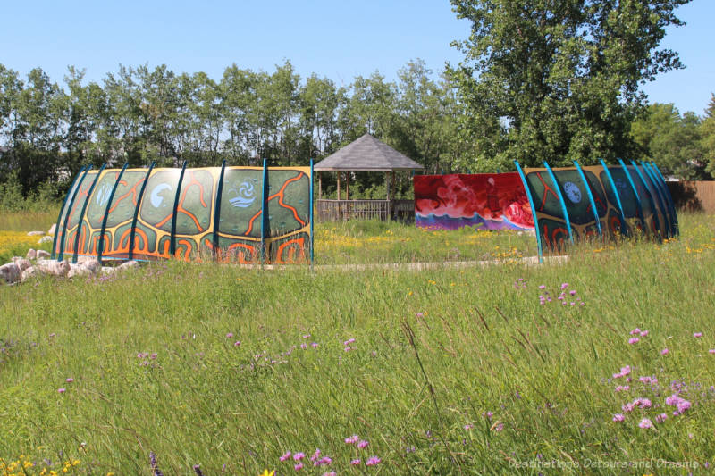 Curved panels painted with murals set in a circle in the midst of a tall grass prairie field
