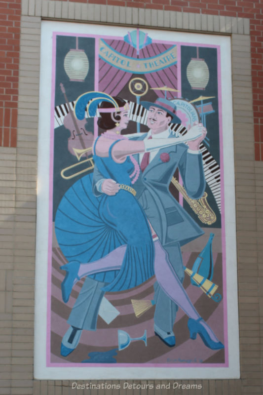 Moose Jaw Murals Dancing On River Street Mural shows 1920s dancing couple with a collage of instruments and party items in the background