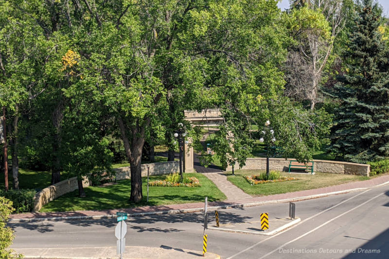 Stone archway with low stone wall on either side with greenery from trees around it is entrance to a city park