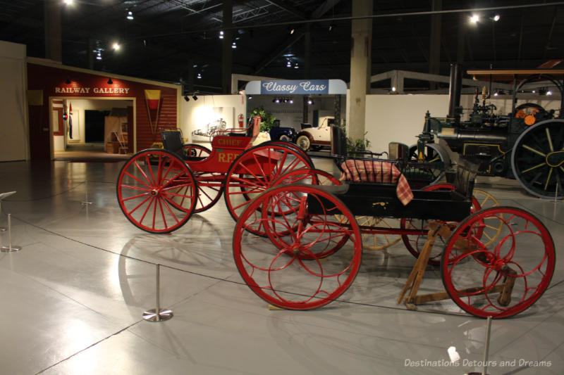 A couple of horse-drawn carriages, without the horses, in the lobby of a museum, in front of the Railway Gallery and the Classy Car Gallery