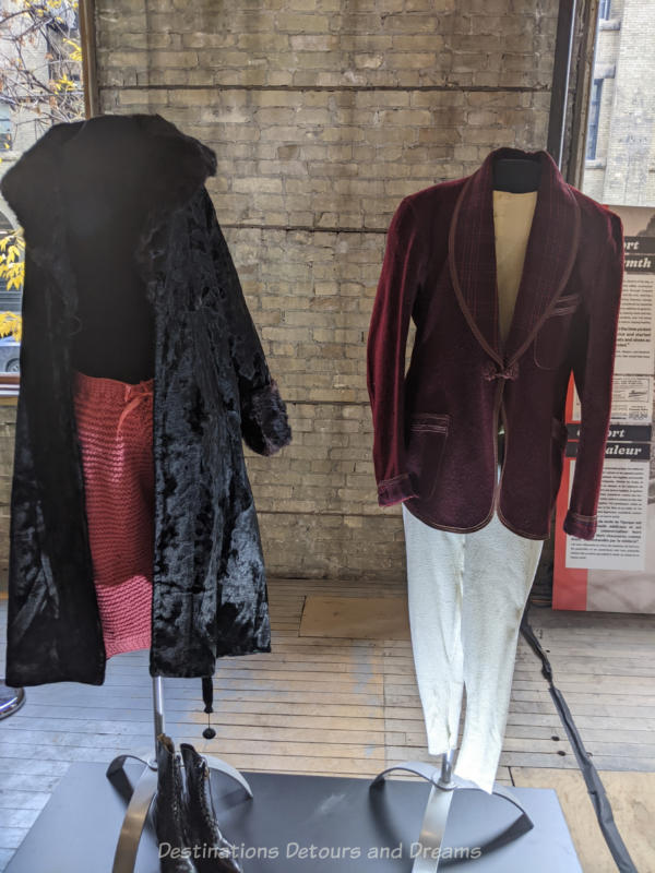 Two mannequins wearing a ladies 1920s black outer coat  and a man's burgundy jacket