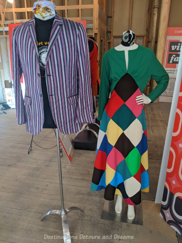 Mannequins weating a purple and grey striped sports jacket and a long polyester dress with green bodice and triangles of many colours in the skirt.