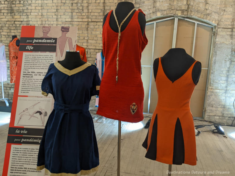 Three mannequins wearing ladies' swimwear from the 1920s - a blue suit with gold trim, a red one with deep cut neck, and an orange one with black pleats added to skirt