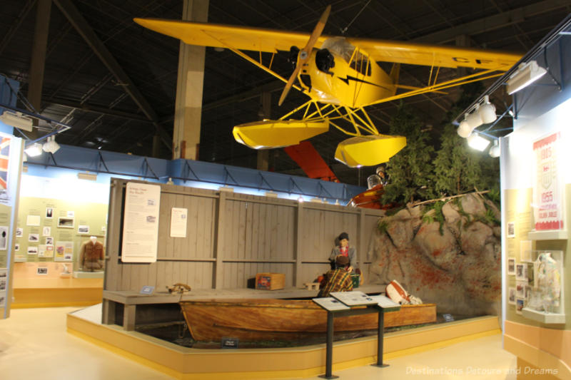 Museum display featuring three types of transportation to remote areas: boat, Piper Cub aircraft,  snowmobile