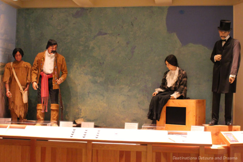 A museum diorama showing a First Nations and Métis couple at one end and European settlers at the other
