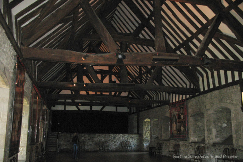 Interior of an surviving old abbey building with stone walls and timbered roof, room empty but for a few chairs along walls and display information on the walls