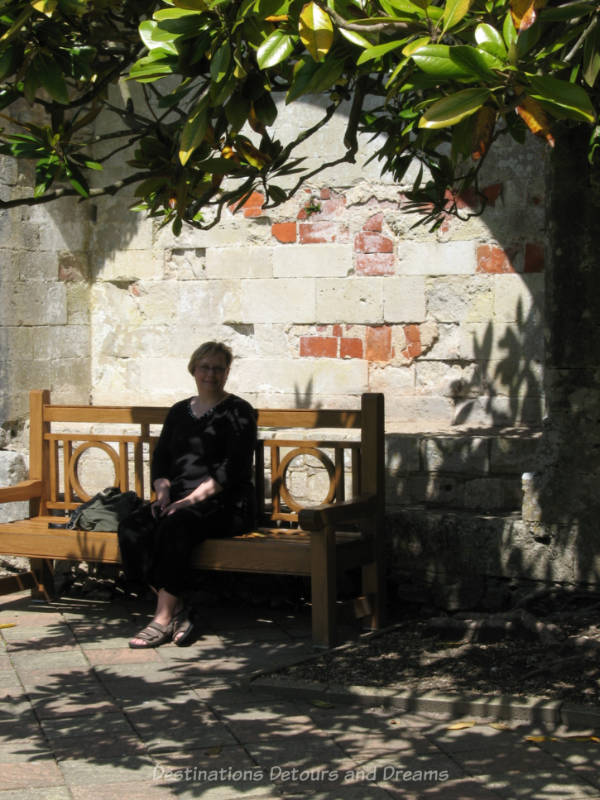 Women sitting on wooden bench in shade of tree with brick wall behind here