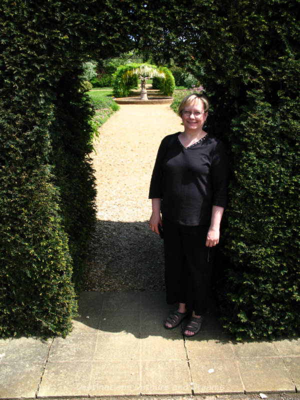 Woman standing in greenery-lined archway leading into a garden