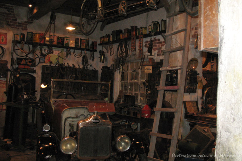 Area in a 1950s garage in a motor museum containing vehicle for service and shelves lined with tools and jars of engine items