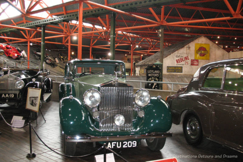Old green roadster with other vintage cars beside it inside a motor museum