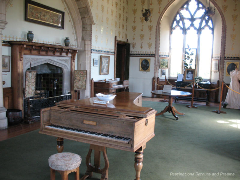 Grand high-ceilinged green-carpeted drawing room in Victorian-era palace house with piano, fireplace, and white and gold wallpaper