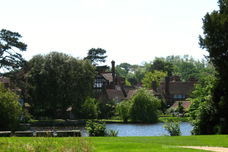 Village of red brick houses among greenery of mature trees as viewed from across a small river